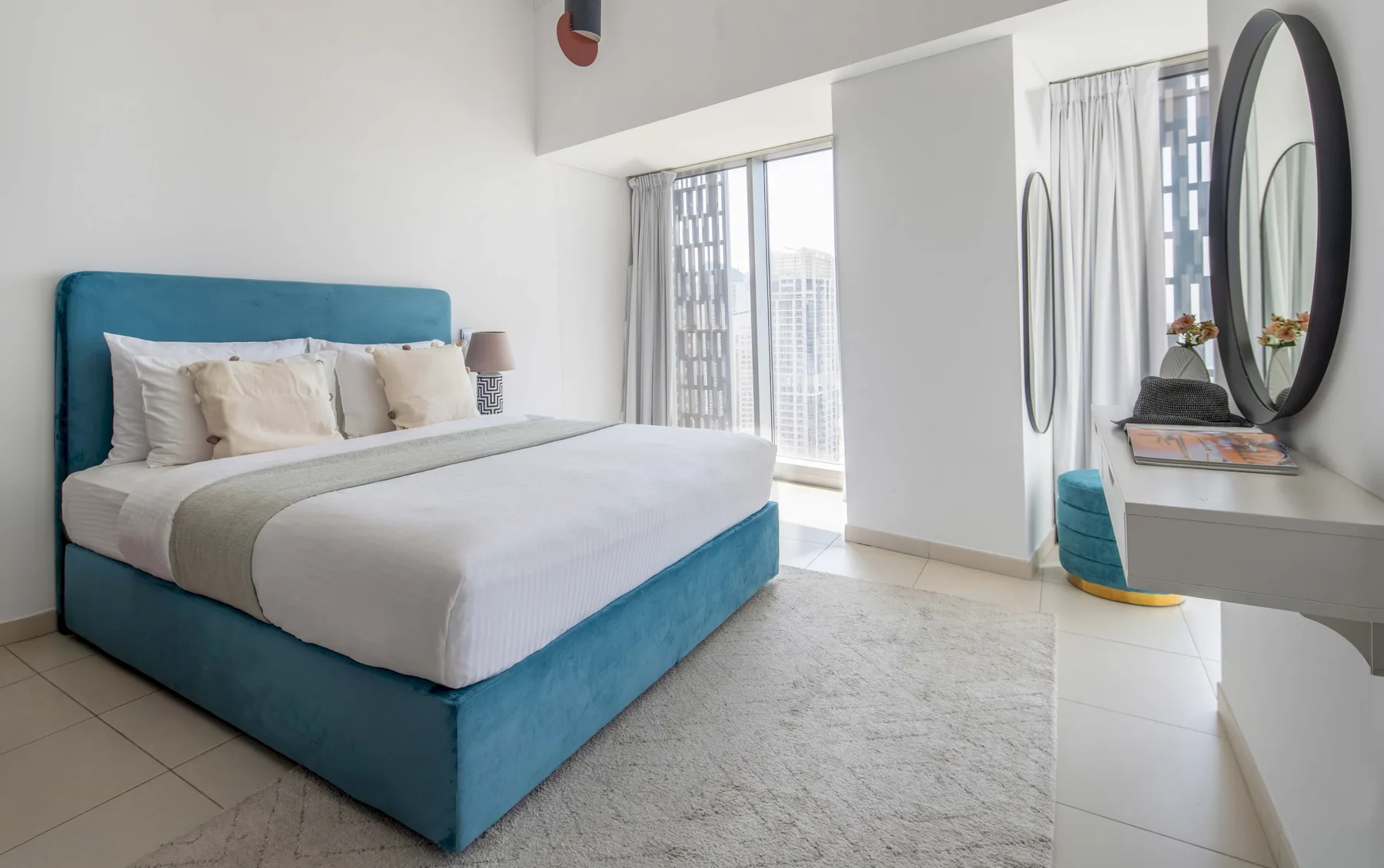 Un dormitorio luminoso con una cama junto a grandes ventanas y un tocador.