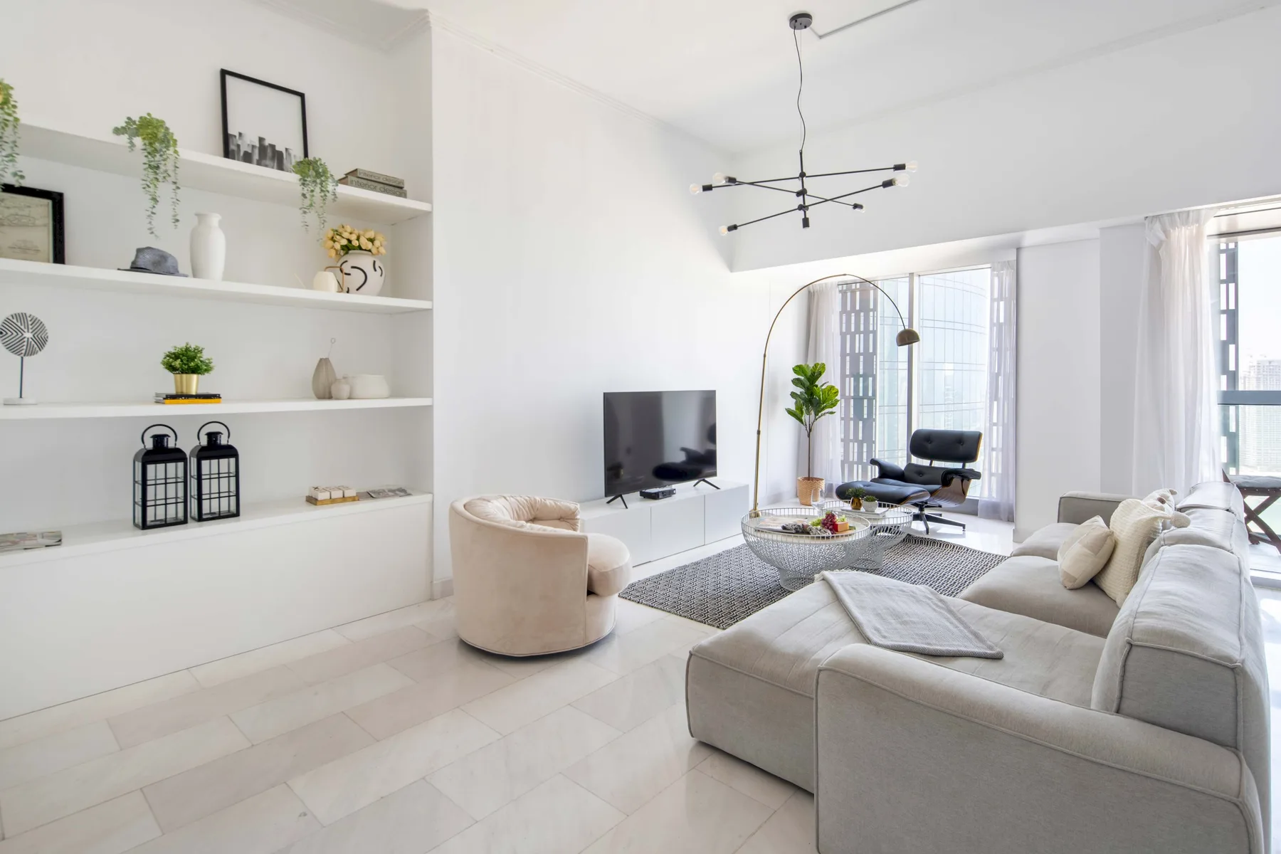 Una sala luminosa con asientos blancos, un televisor y ventanales.