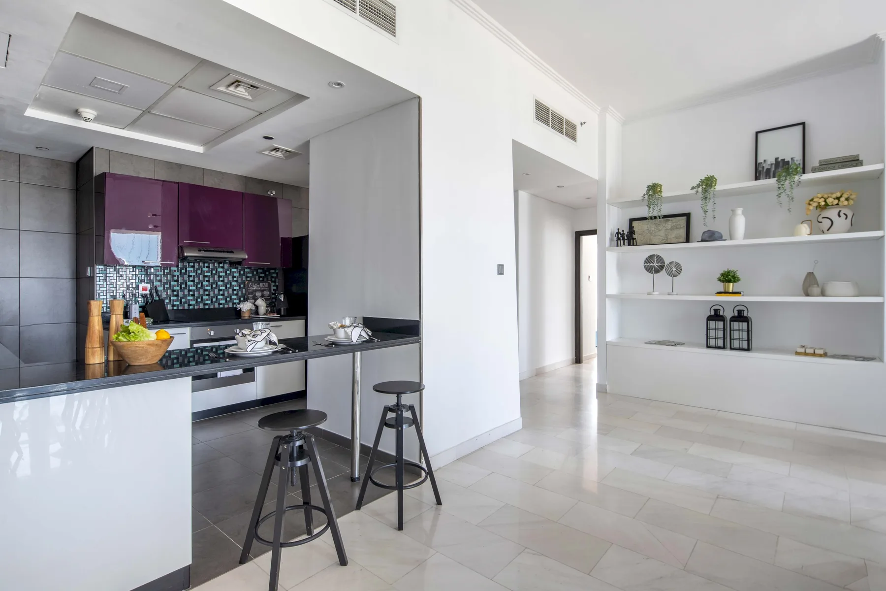 Una cocina luminosa da a un pasillo, con estantes abiertos junto a la pared.