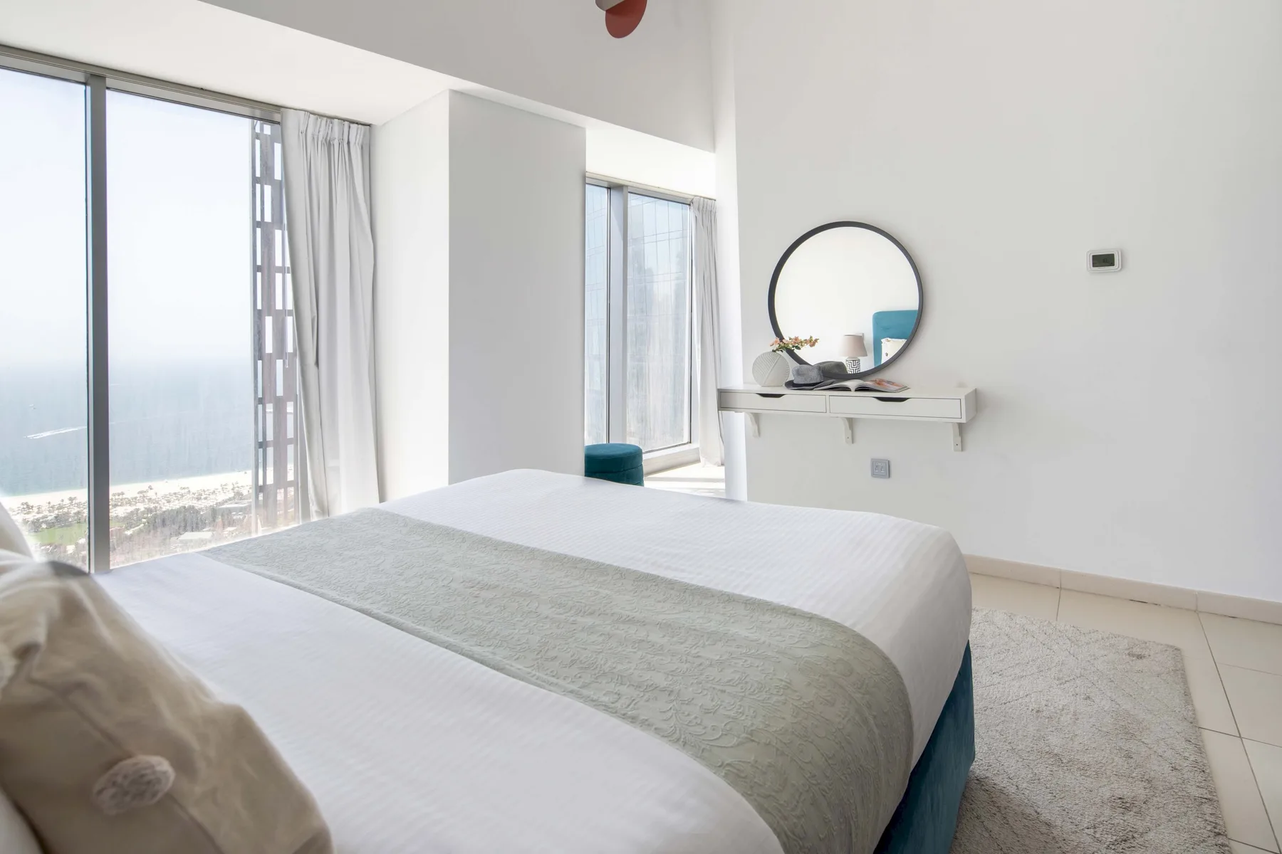 Un dormitorio luminoso con una cama arreglada y un espejo redondo sobre un estante de pared.