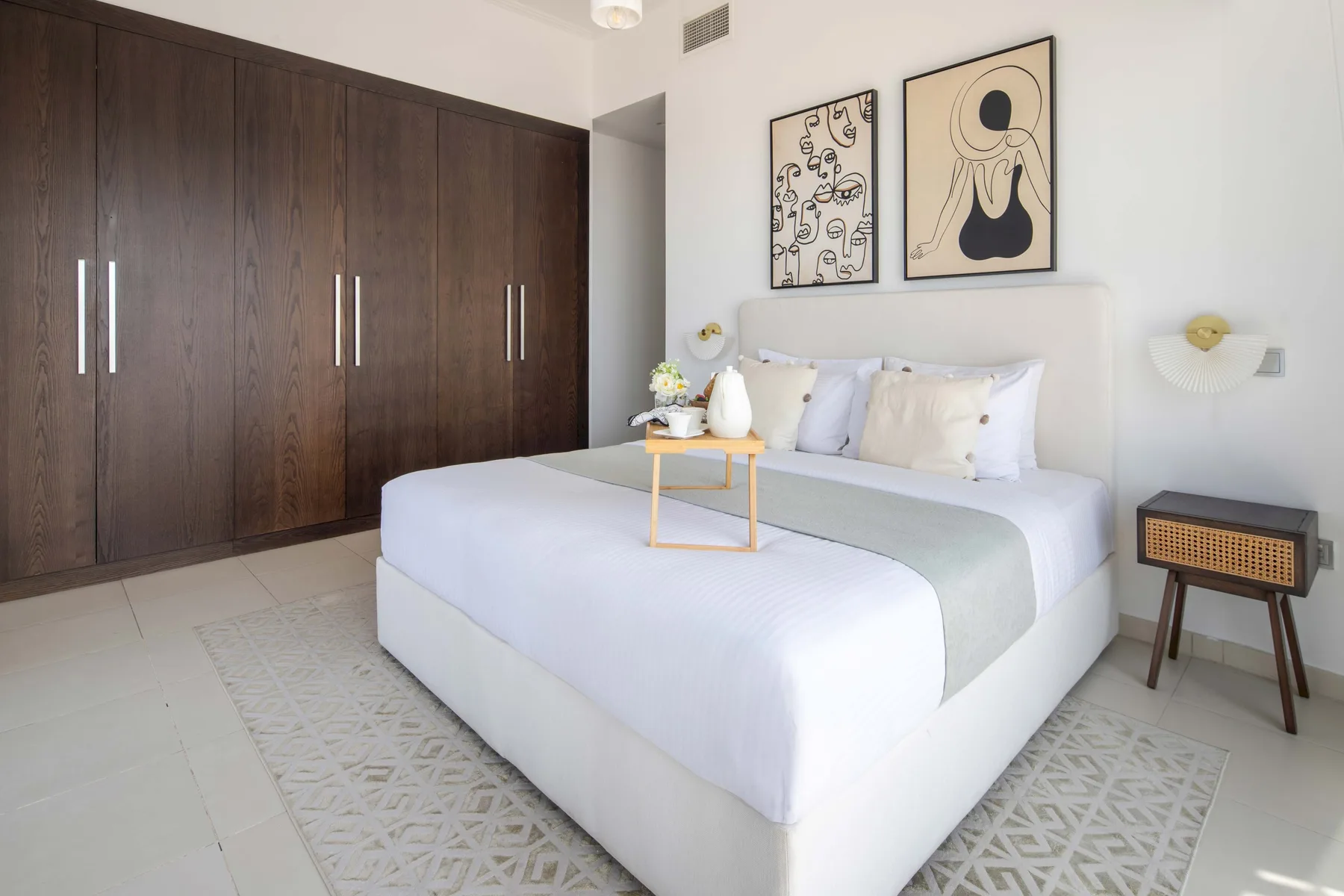 Un dormitorio luminoso con una cama, armarios oscuros y cuadros enmarcados.