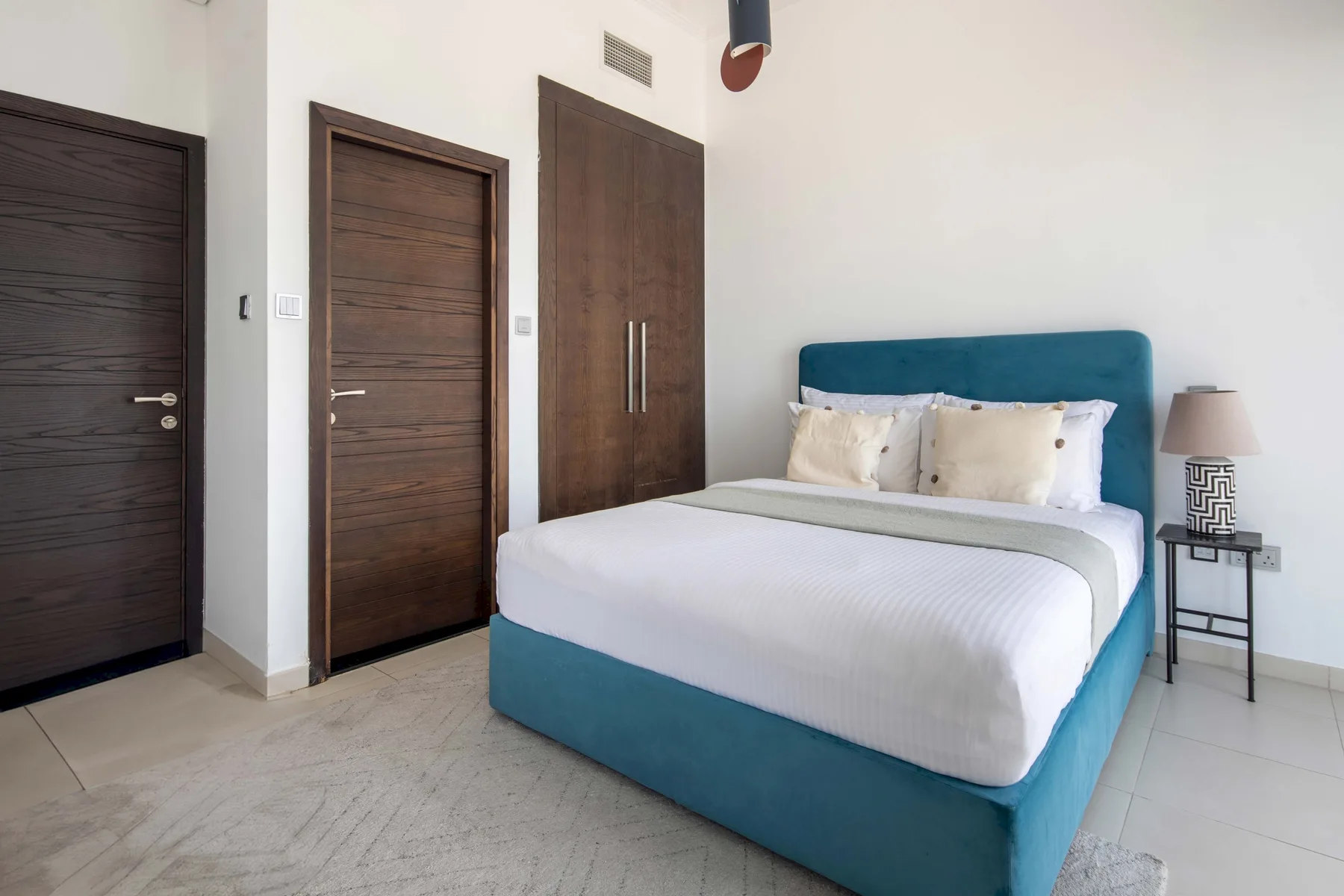 Un dormitorio con una cama color turquesa, ropa de cama blanca y puertas de madera oscura.