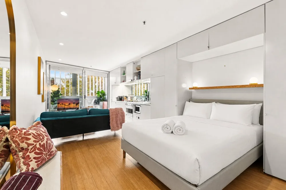 Una habitación luminosa y diáfana combina una cama, una zona de estar y una cocina compacta.