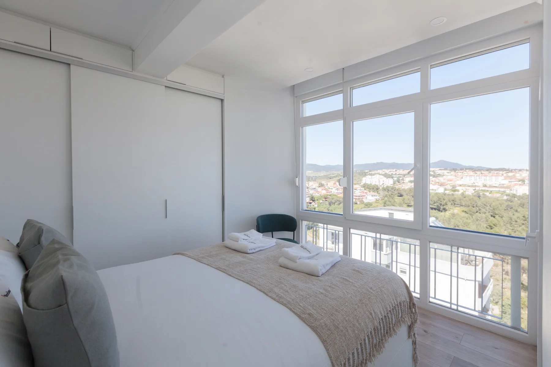 A bright bedroom with a bed beside large windows overlooking the surrounding area.