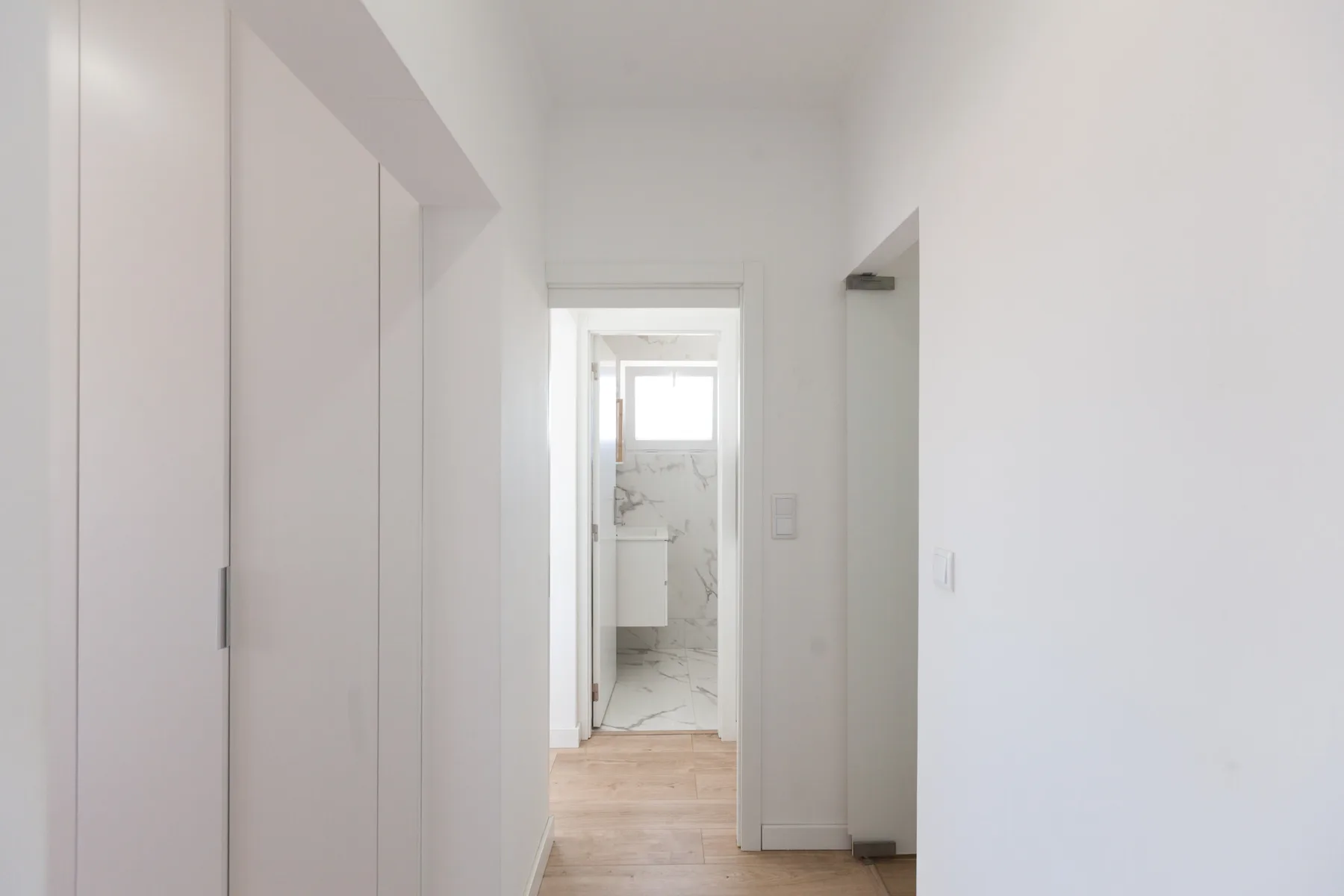 A bright hallway leads to a bathroom with a marble-patterned wall.