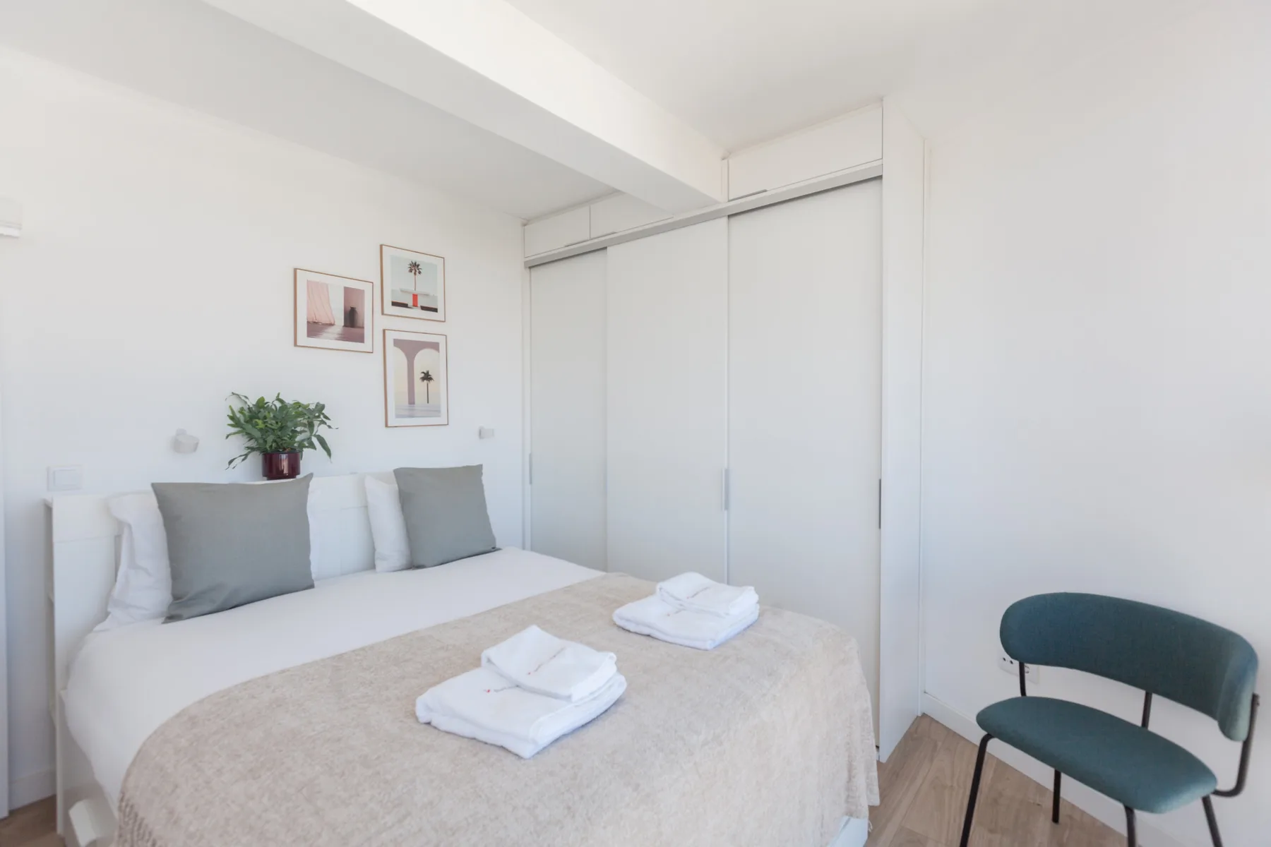 A bright bedroom with a neatly made bed and a teal chair.