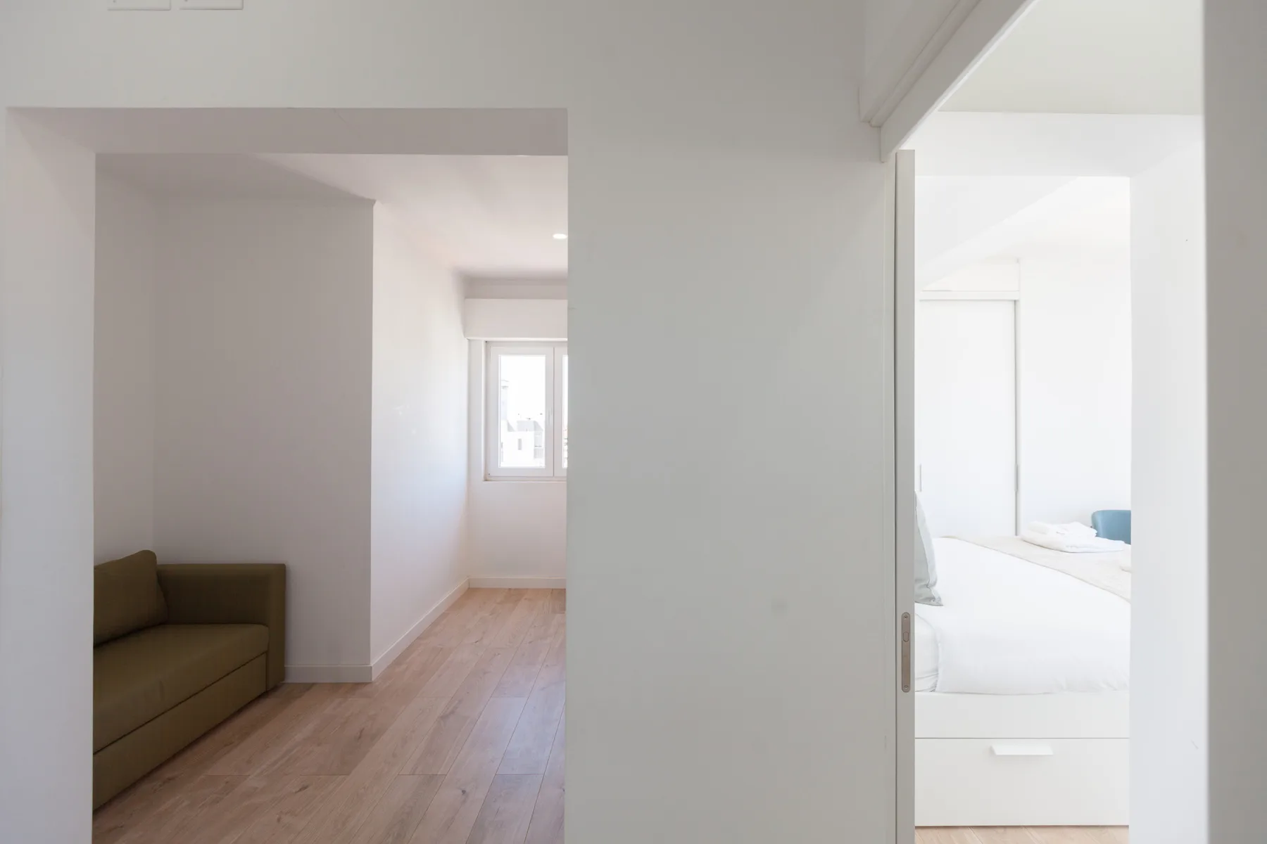 A bright apartment interior with a hallway leading toward a small seating area.
