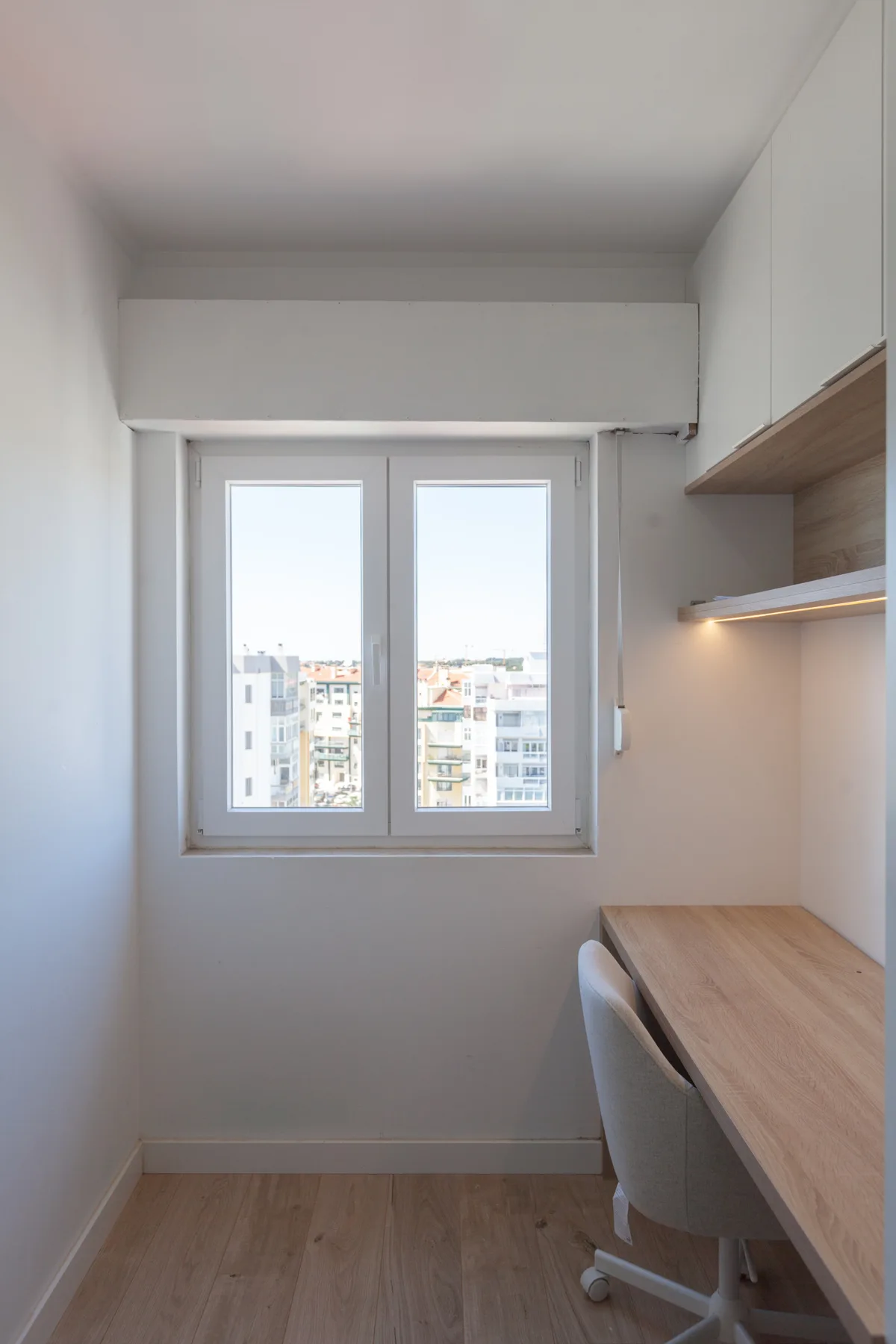 A compact workspace with a desk and window overlooking nearby buildings.