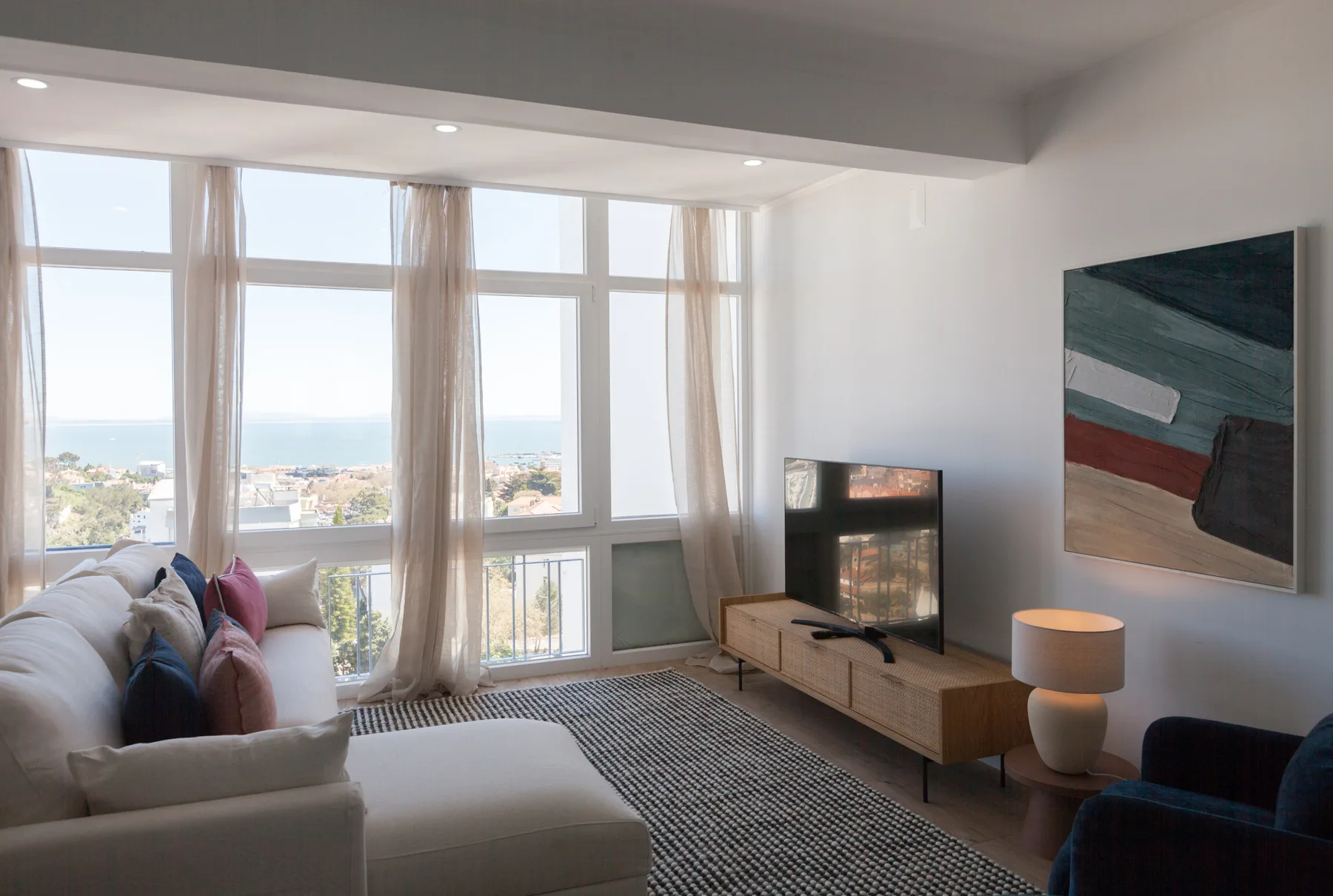 A bright living room with large windows, a sofa, and a television.