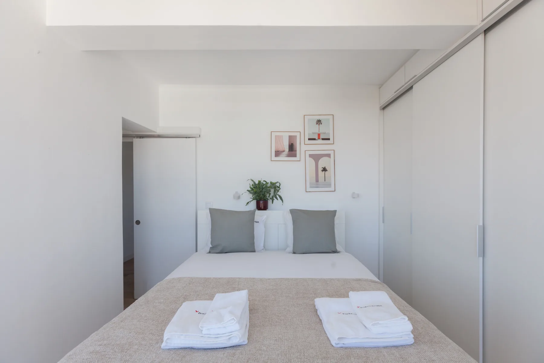 A bedroom with a neatly made bed and framed prints on the wall.