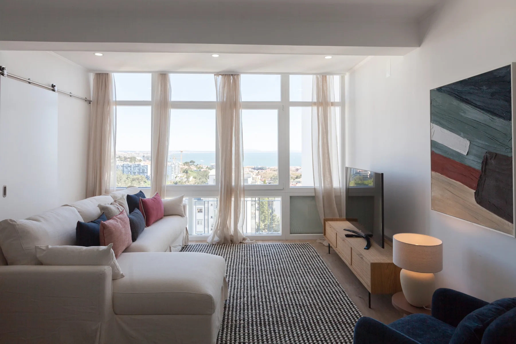 A bright living room with seating arranged beside large windows overlooking the sea.