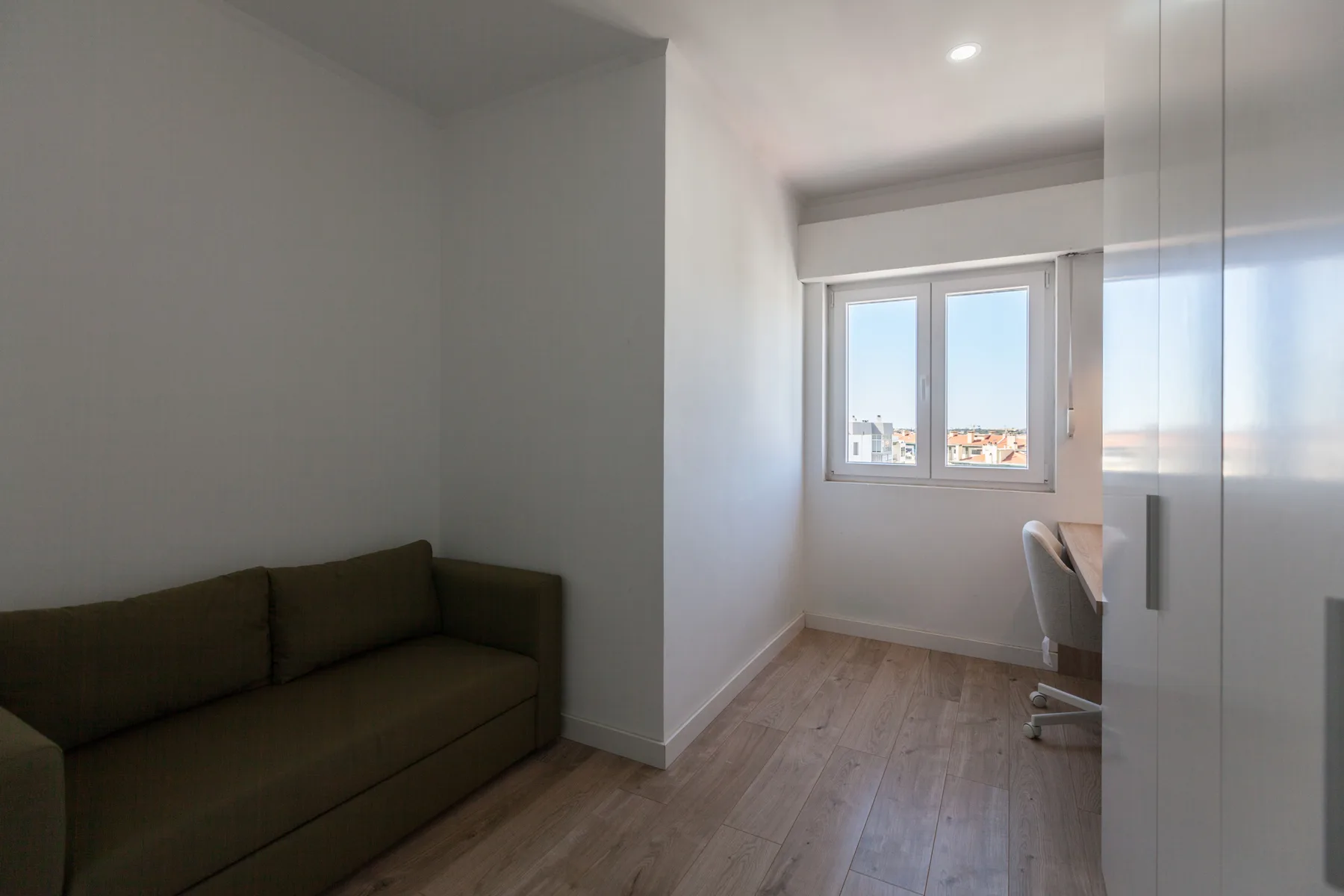 A small room with a dark sofa beside a window and desk.