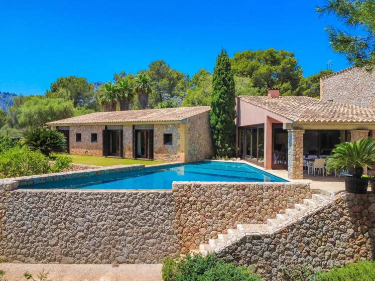 A stone house with a swimming pool and landscaped gardens under a clear blue sky.