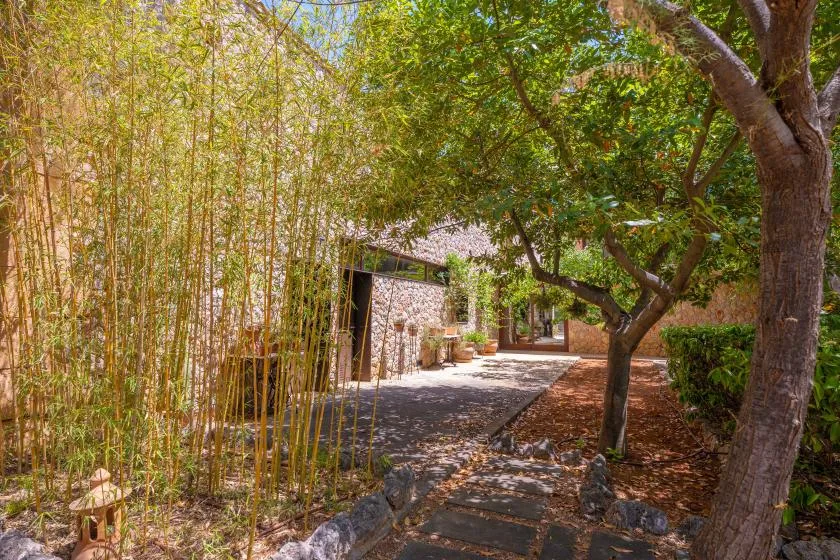 A garden path winds beneath leafy trees beside a stone building.