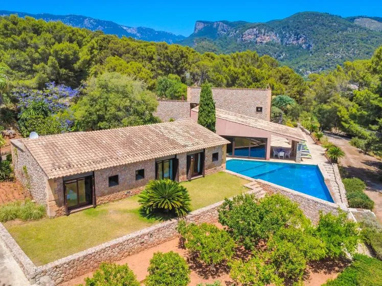 A stone house and blue swimming pool sit among green hills.