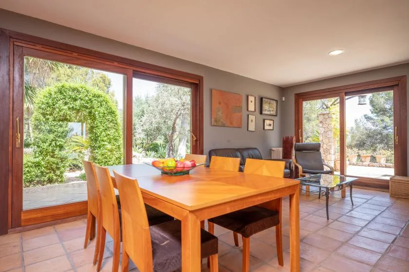 Dining area with a wooden table and large windows overlooking greenery.