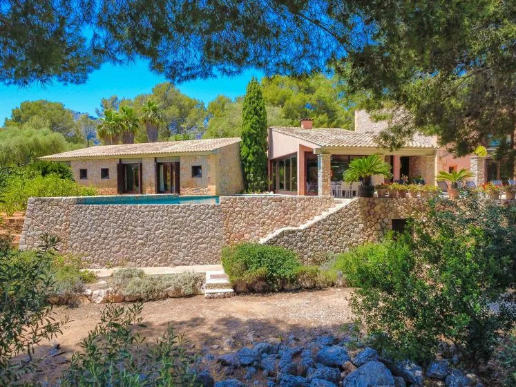 A stone house and swimming pool sit among trees and landscaped gardens.