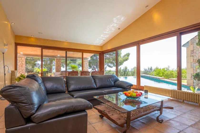 A bright living room with dark seating and a glass coffee table beside large windows.