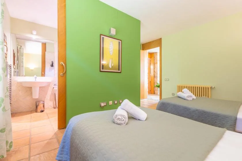 A bedroom with two beds, a green accent wall, and an open bathroom doorway.