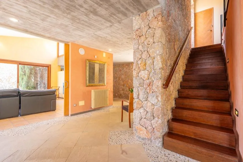 A bright living room opens onto a staircase beside a stone wall.
