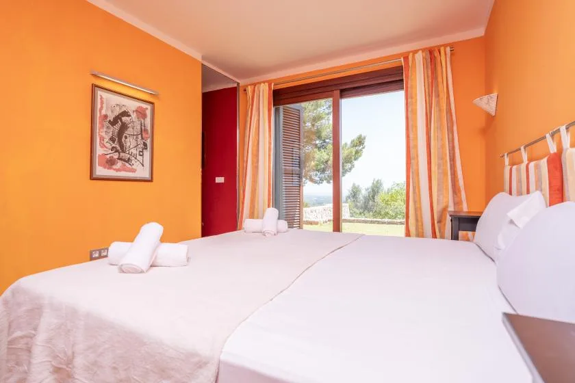 An orange bedroom with white bedding and a large window overlooking greenery.