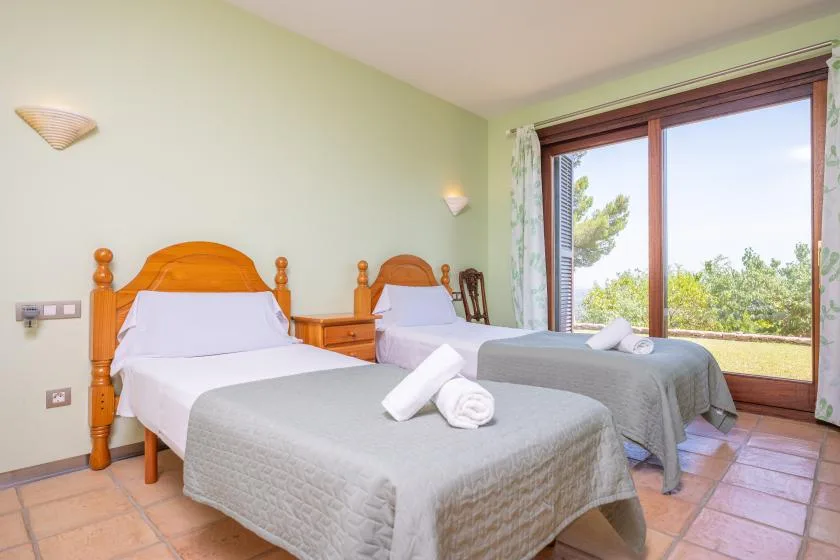 A bedroom with two single beds beside a large window overlooking greenery.