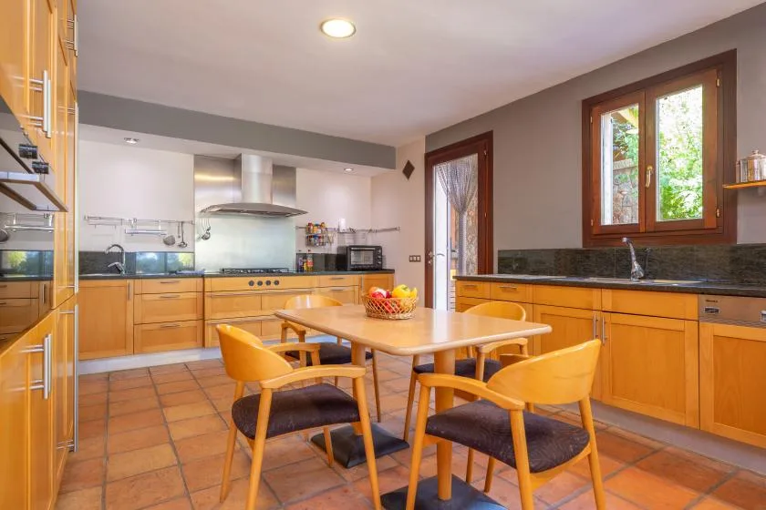 A bright kitchen with wooden cabinets, a central table, and a window.