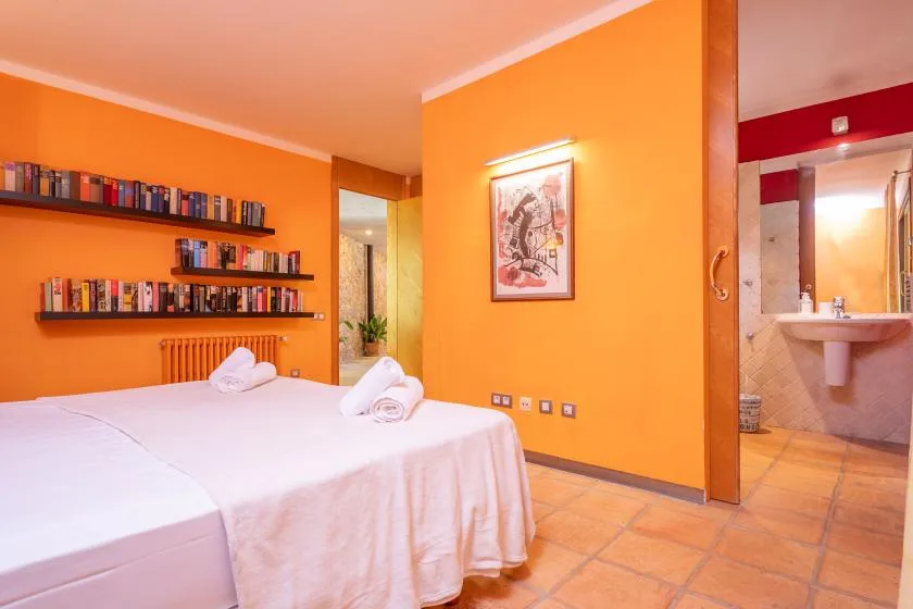 A bedroom with white bedding, wall shelves, and an open doorway to a bathroom.