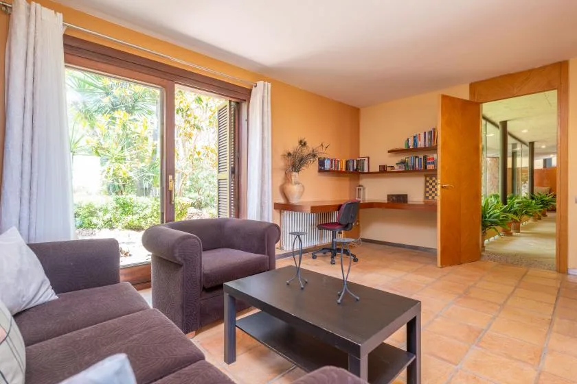 A warm-toned room with seating, a desk, and large windows overlooking greenery.