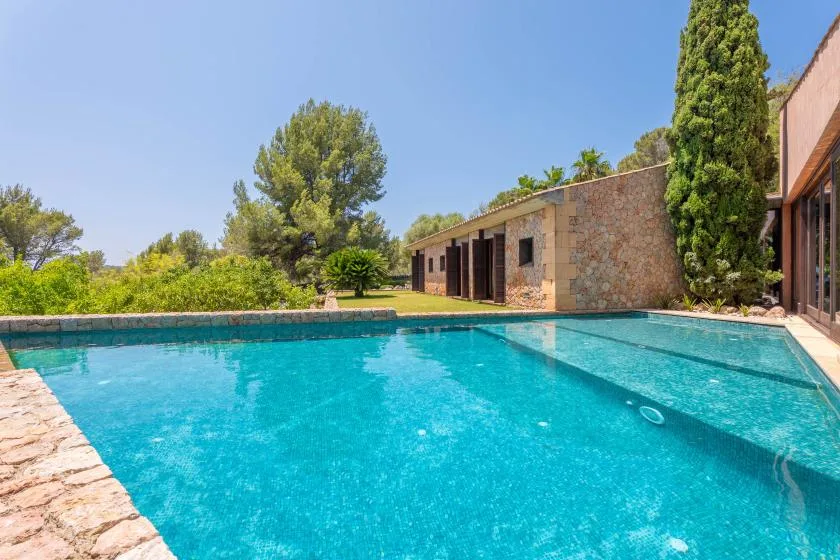 An outdoor swimming pool beside a stone building and leafy trees.