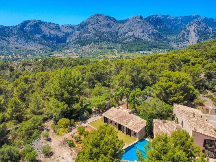 An aerial view of homes and a blue swimming pool surrounded by forest and mountains.