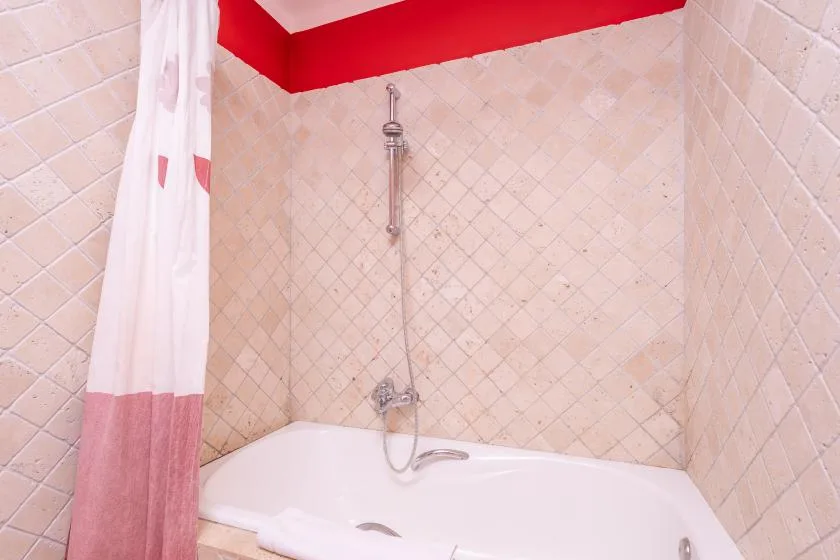 A tiled bathroom shower is positioned above a white bathtub with a curtain.