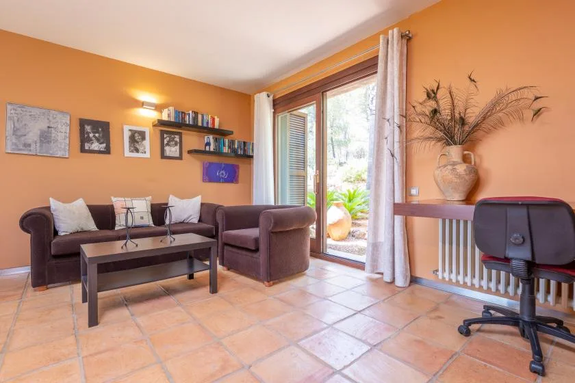 A living room with seating, a coffee table, and a glass door opening to a garden.