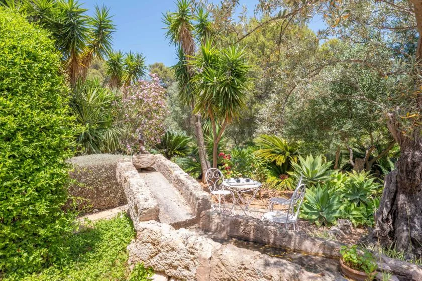 A garden patio with stone seating and a small round table among lush plants.