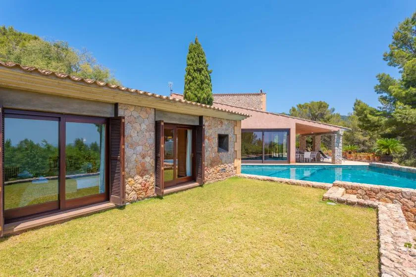 A stone house opens onto a grassy yard beside a swimming pool.