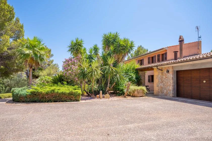 A house and garage stand beside a paved driveway and landscaped garden.
