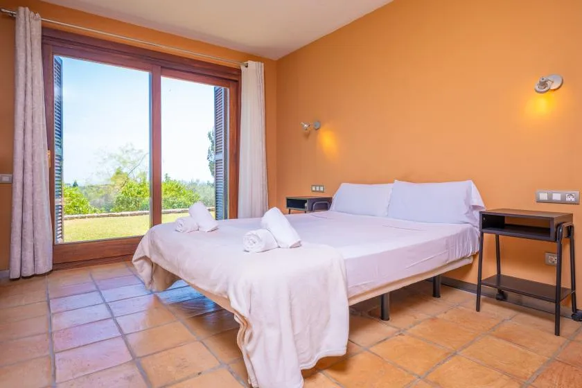 A bedroom with a bed beside a large glass door opening onto greenery.