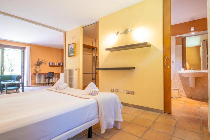 A bright bedroom with a bed, wall shelves, and an open doorway to a bathroom.
