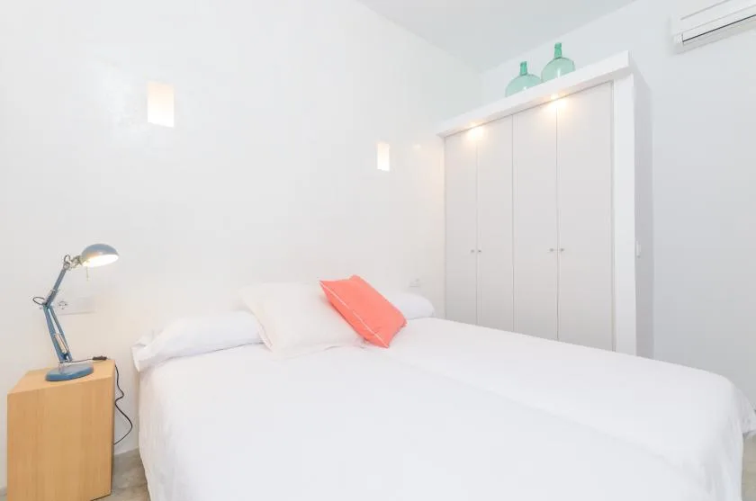 A bright bedroom with a white bed and built-in wardrobe.