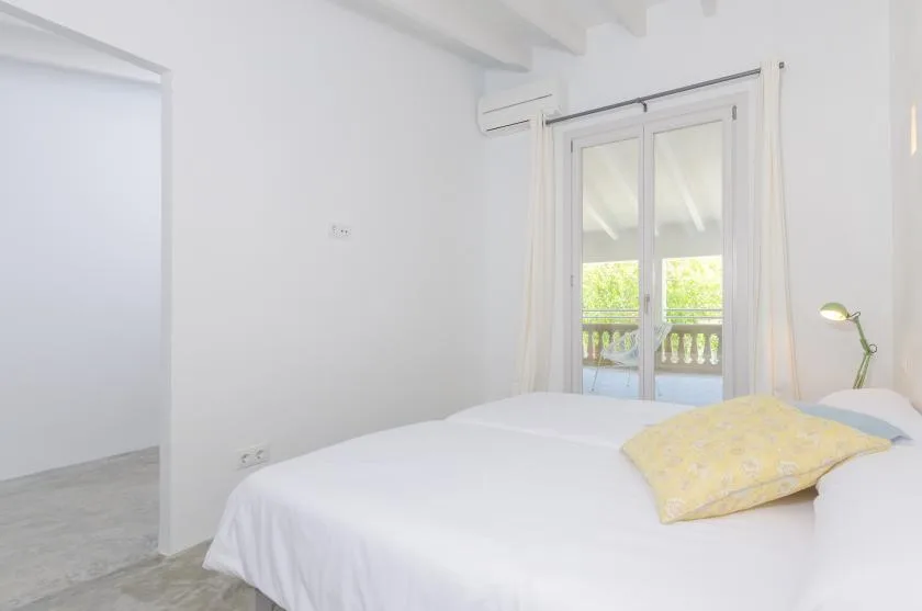 A bright bedroom with a bed beside glass doors opening onto a balcony.