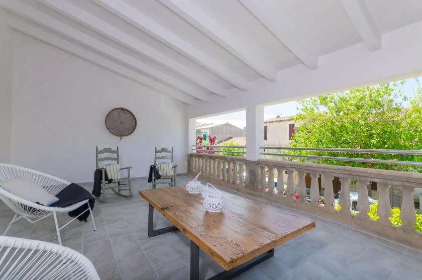 A covered outdoor terrace with a wooden table and seating overlooks leafy trees.