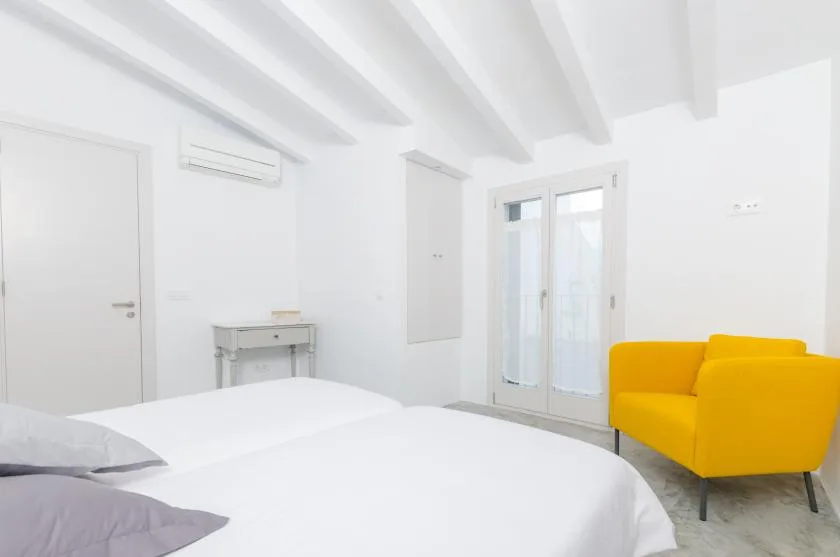A bright bedroom with white bedding and a yellow armchair.