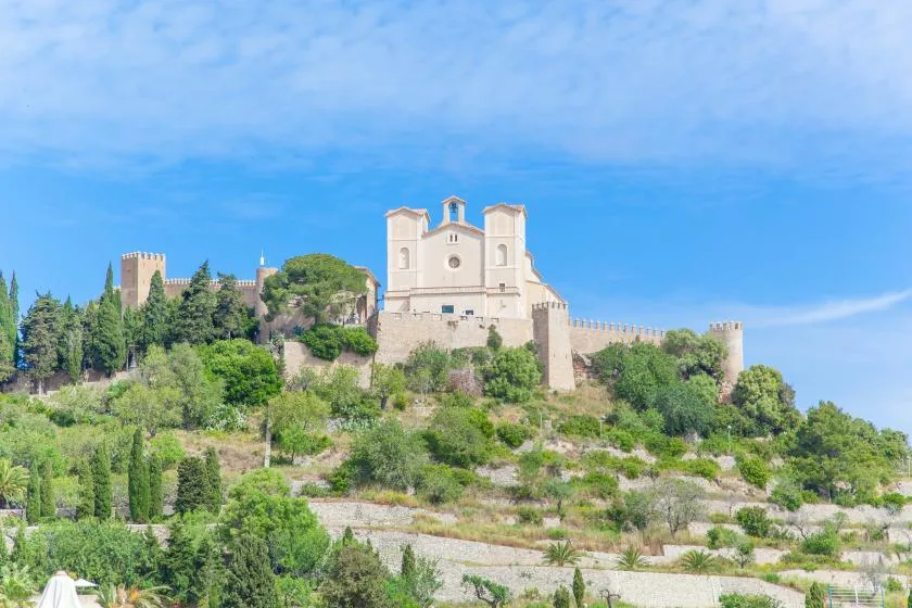 A hilltop stone fortress with a pale church-like building overlooks green terraced slopes.