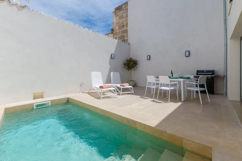 An outdoor pool beside a paved patio with lounge seating and a dining table.