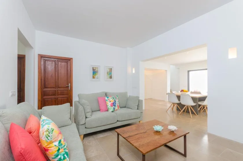 A bright living room with seating, a wooden coffee table, and a dining area beyond.