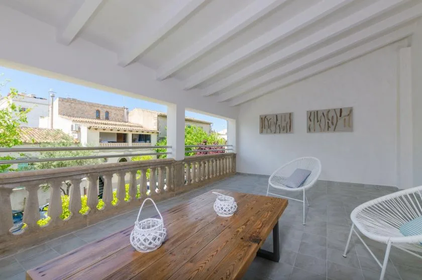 A covered terrace with a wooden table, woven seating, and views of neighboring buildings.