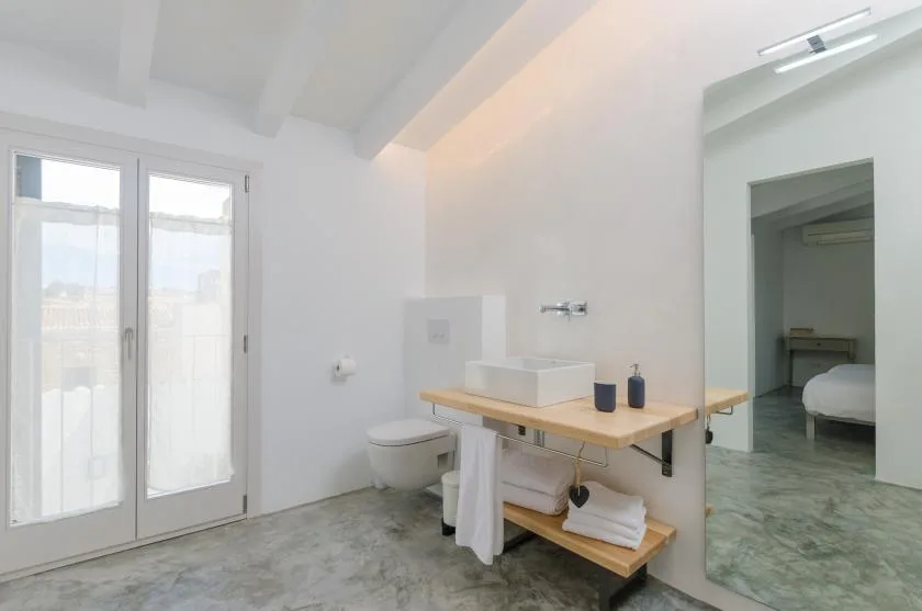 A bright bathroom with a sink, toilet, and glass doors opening onto a balcony.