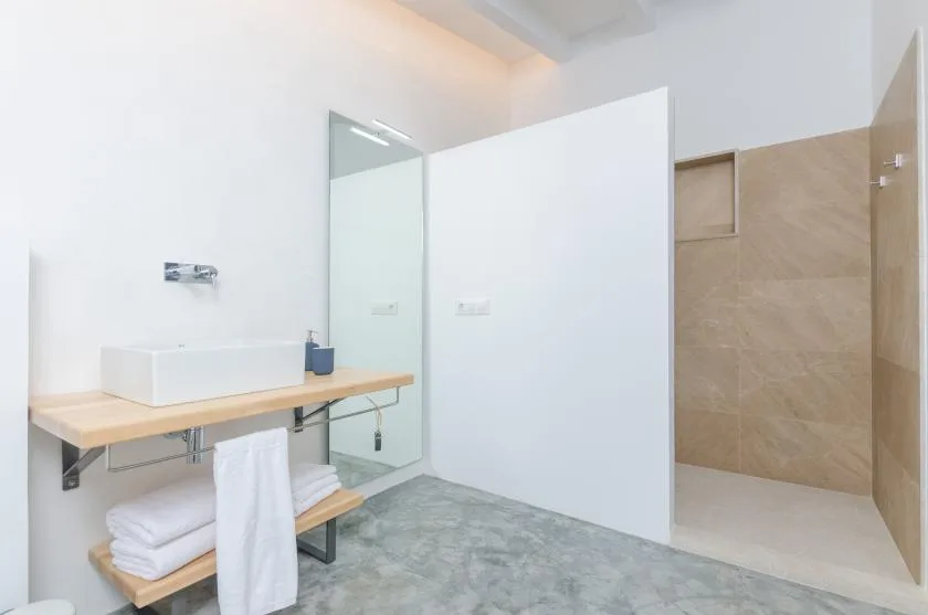 A bright bathroom with a wall-mounted sink, mirror, and open shower area.