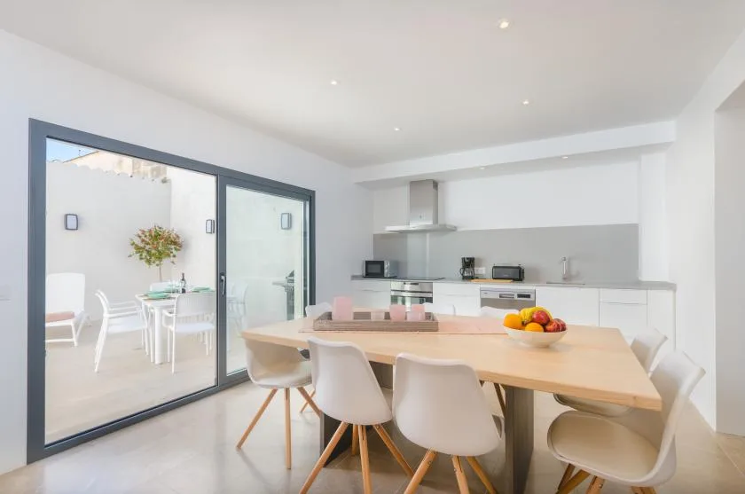 A bright dining area with a long table beside a modern kitchen and glass doors.