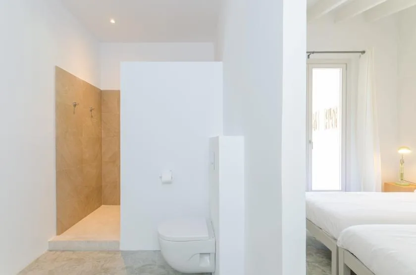 A bright bathroom with a walk-in shower beside a sleeping area.